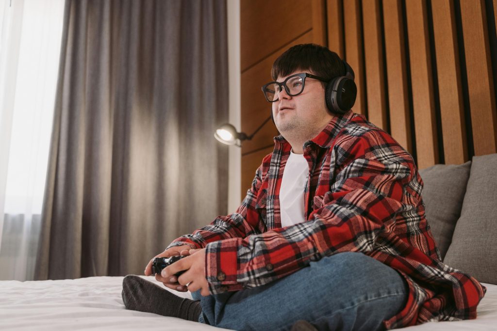 Man in Red White and Black Plaid Dress Shirt and Blue Denim Jeans Sitting on Bed